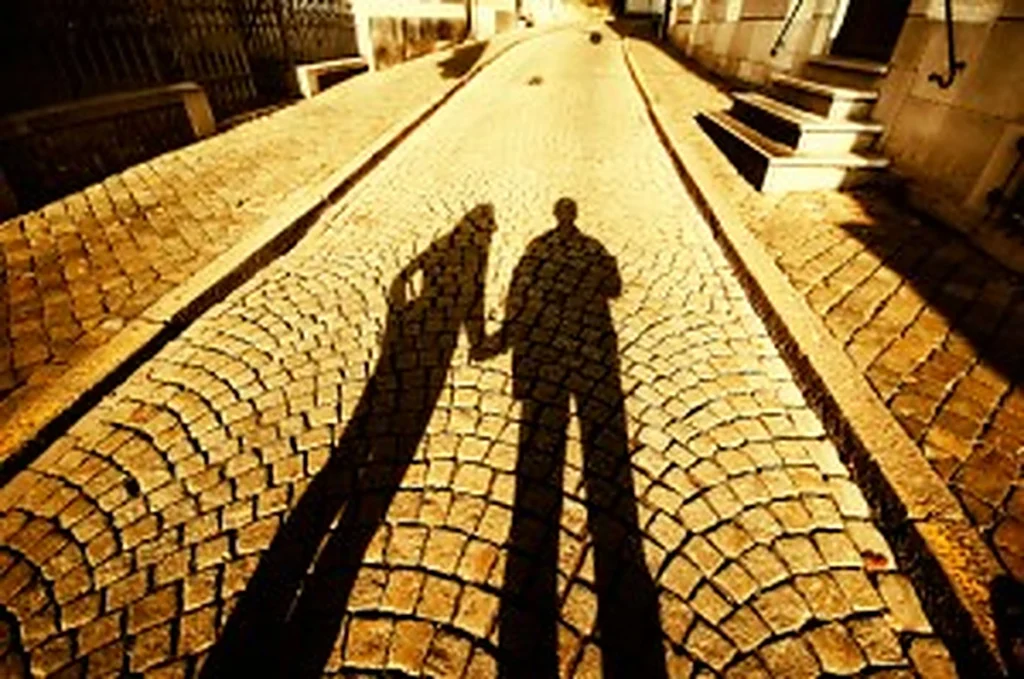 Sombras alargadas de dos personas tomadas de la mano proyectadas sobre una calle de adoquines al atardecer