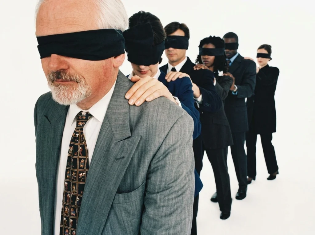 Fila de ejecutivos con los ojos vendados avanzando en fila, cada uno con la mano en el hombro del anterior