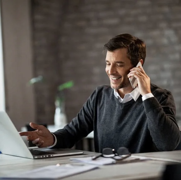 Profesional sonriente hablando por teléfono frente a su computadora